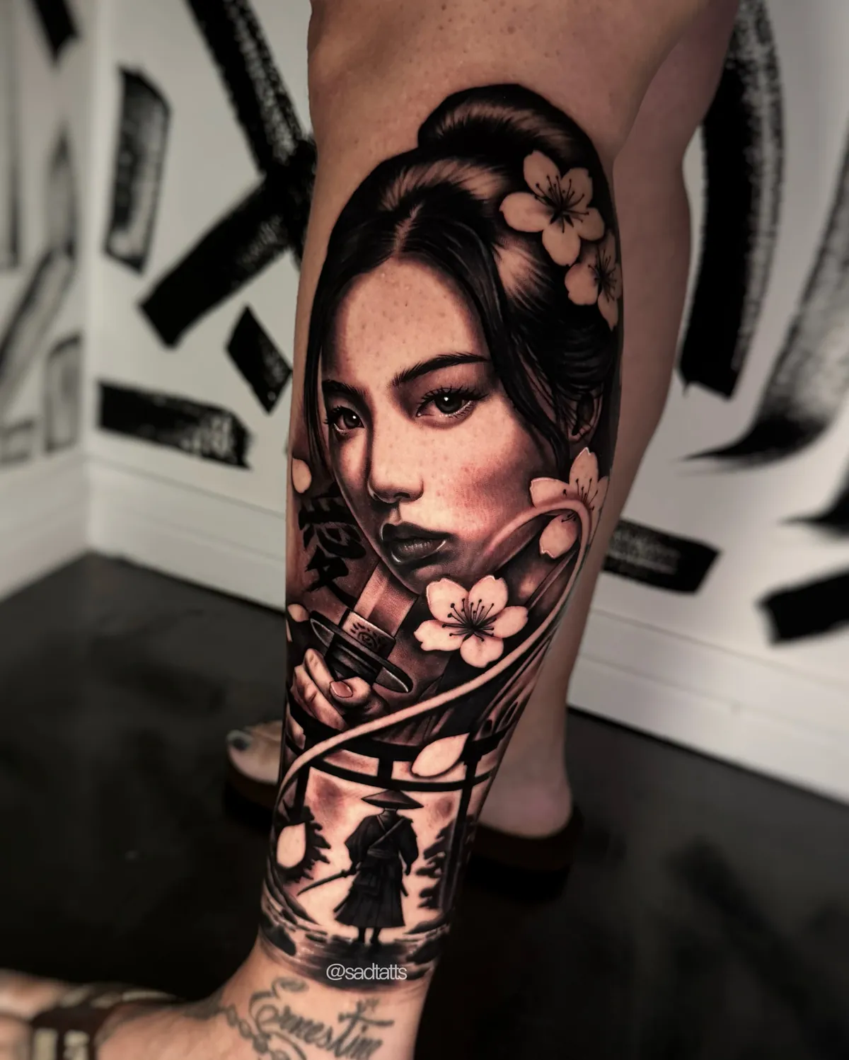 Black and grey realism tattoo of a geisha with cherry blossoms on a calf, in Dre's studio