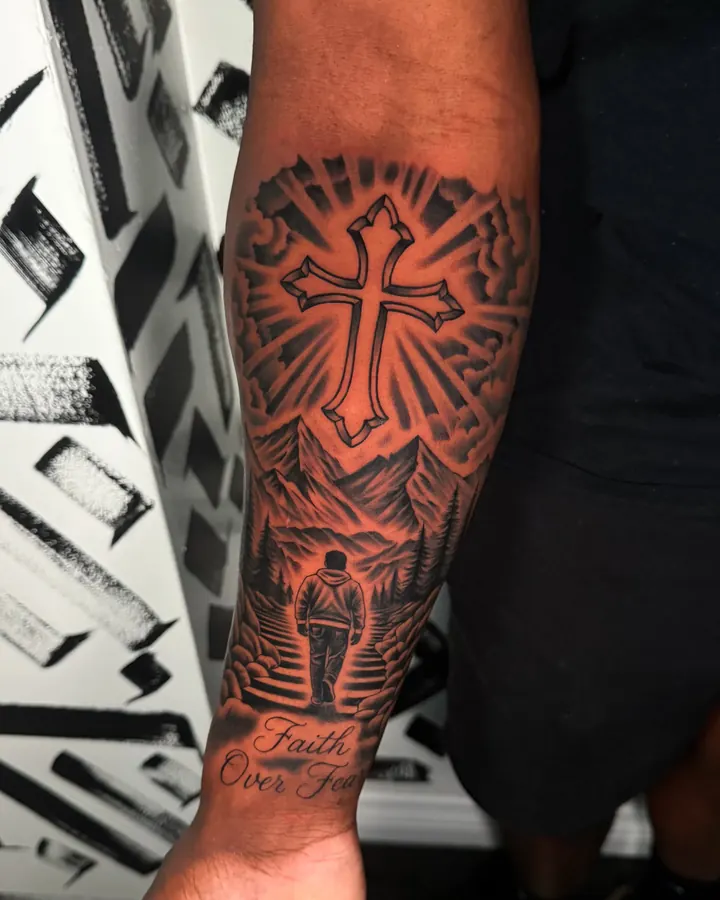 Black and grey tattoo by Dre: Cross, mountains and Faith Over Fear, forearm