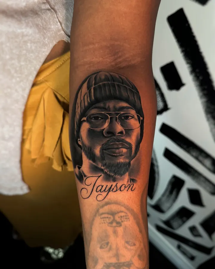 Black and grey tattoo by Dre: Portrait with glasses and beanie, forearm